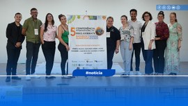 Foto colorida, com dez pessoas em pé e sorridentes, e ao meio o banner do evento.