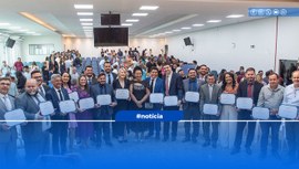 Foto colorida, várias pessoas em pé e sorridentes, posando para foto com certificado na mão.