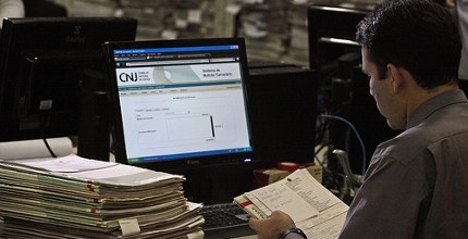 Servidor diante de processos trabalhando. Tela do computador escrito CNJ.